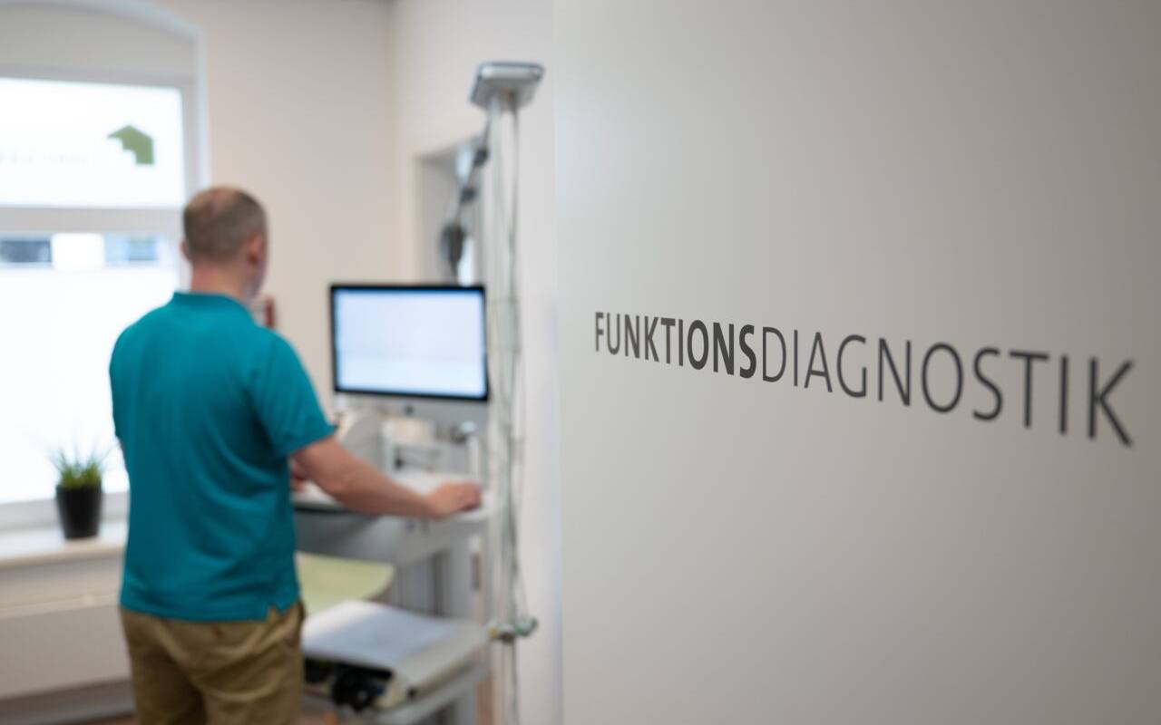 Ein Arzt führt in ein Behandlungszimmer ein funktionelles Gerät. Auf einer Schrift steht Funkionsdiagnostik.