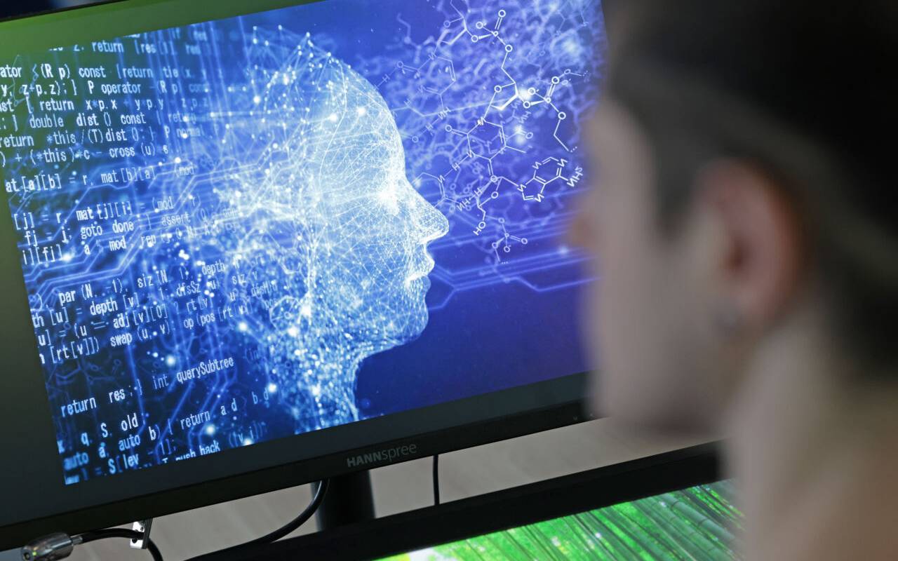 Eine Person sitzt vor einem Bildschirm, auf dem zu erkennen ist, dass es neben dem menschlichen Kopf auch verschiedene Ströme gibt, die fließen. Eine Art Symbolbild für Künstliche Intelligenz