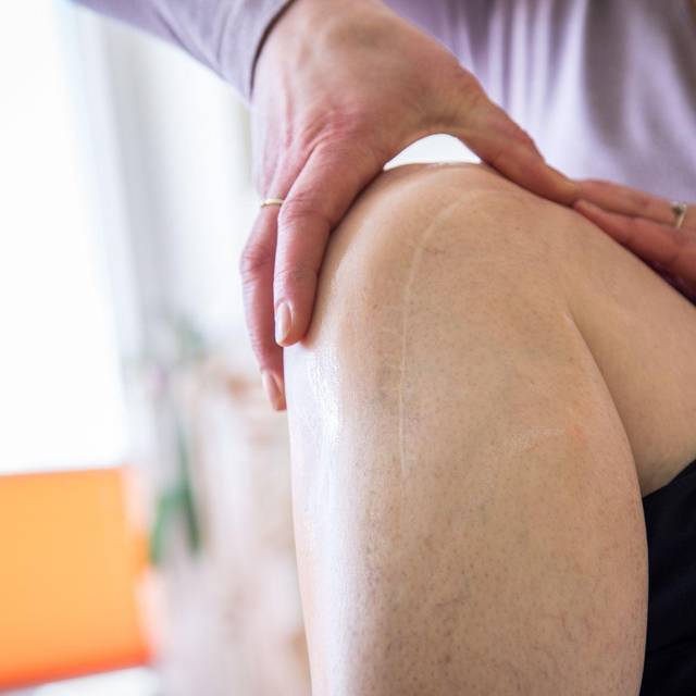 Eine Frau massiert eine Operationsnarbe am Knie