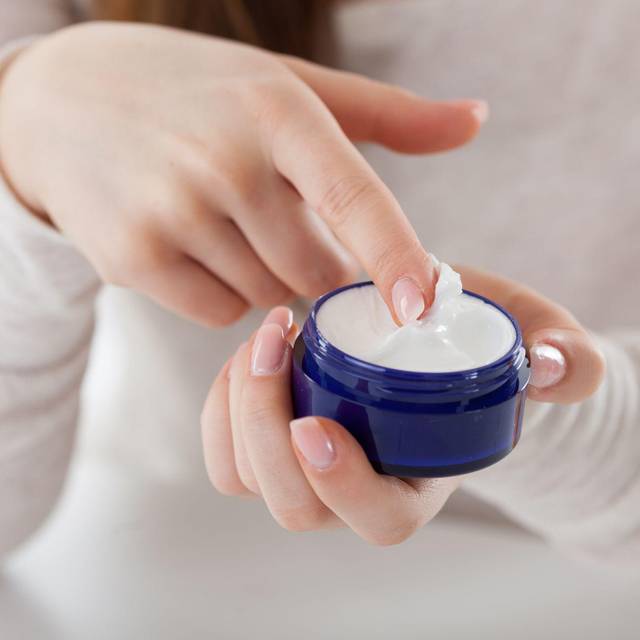 Eine Frau streicht mit dem Finger durch eine Cremedose