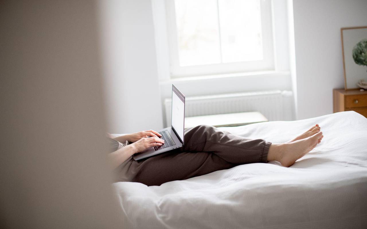 Eine Frau sitzt mit Laptop im Bett