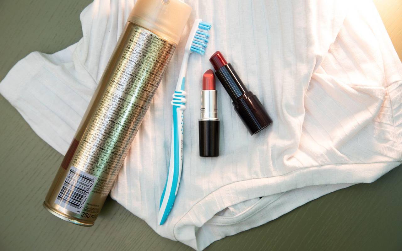 Lippenstift, Haarspray und eine Zahnbürste liegen auf einem Shirt