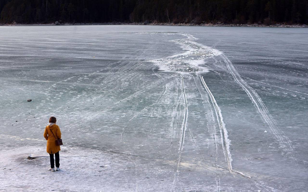 Eine Frau steht am zugefrorenem See nahe einer Einbruchstelle