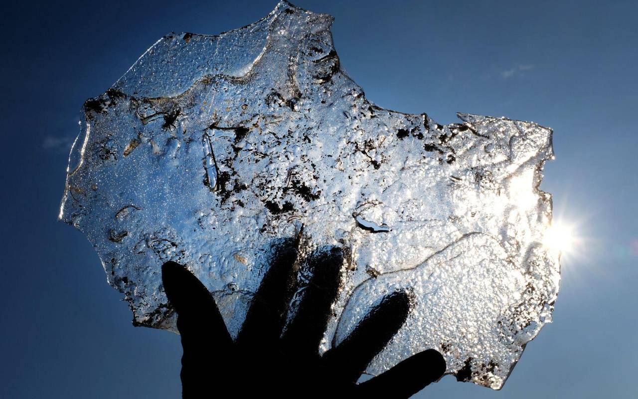 Eine Hand hält eine Eisplatte vor blauem Himmel