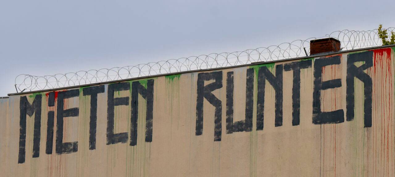 Der Schriftzug "Mieten runter" ist an der Wand eines Miethauses mit Graffiti beschmiert