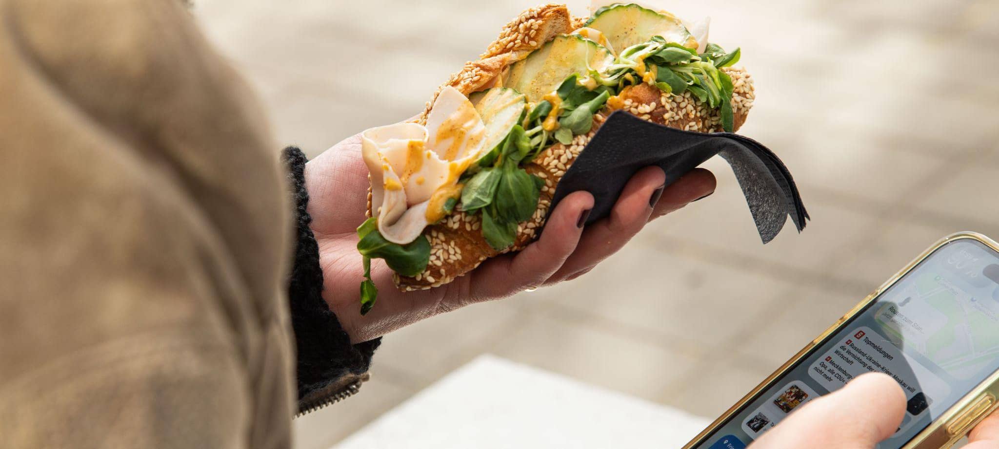 Eine Frau hält ein gefülltes Puten-Croissant und ihr Handy